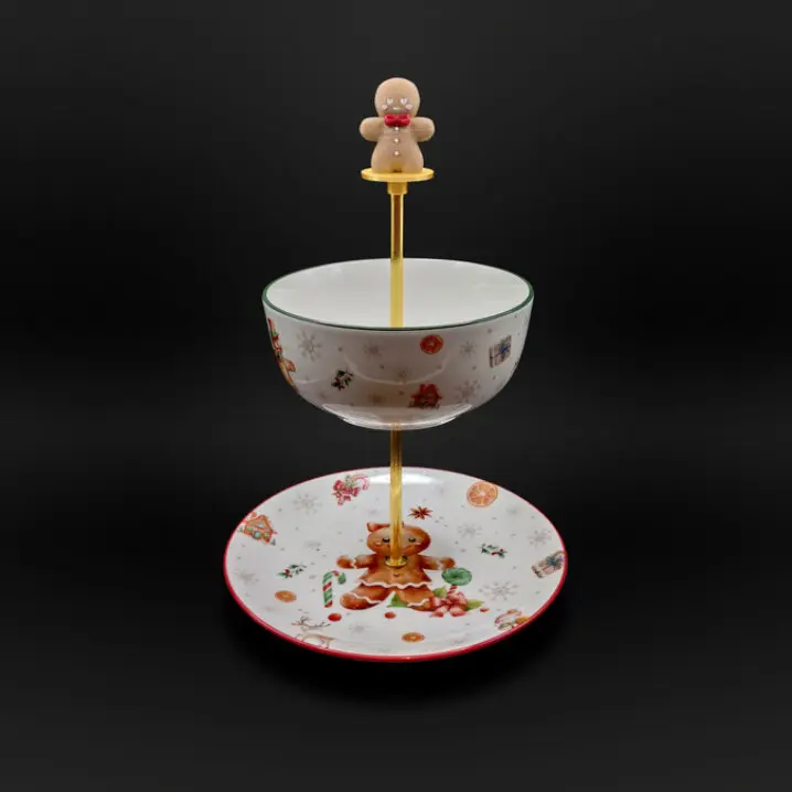 Zweistufige Weihnachts-Etagere mit goldfarbener Stange und Lebkuchenmann-Griff; oben weiße Schale mit grünem Rand und Weihnachtsmotiven, unten weißer Teller mit rotem Rand und Lebkuchenmann-Dekor, vor schwarzem Hintergrund.